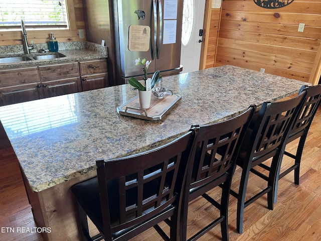 kitchen featuring wooden walls, light wood-type flooring, a breakfast bar, and stainless steel fridge