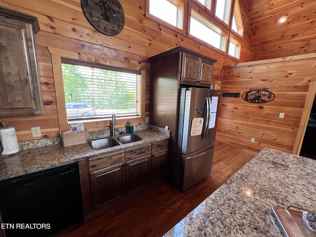 kitchen with sink, dark wood-type flooring, black dishwasher, stainless steel fridge, and wood walls