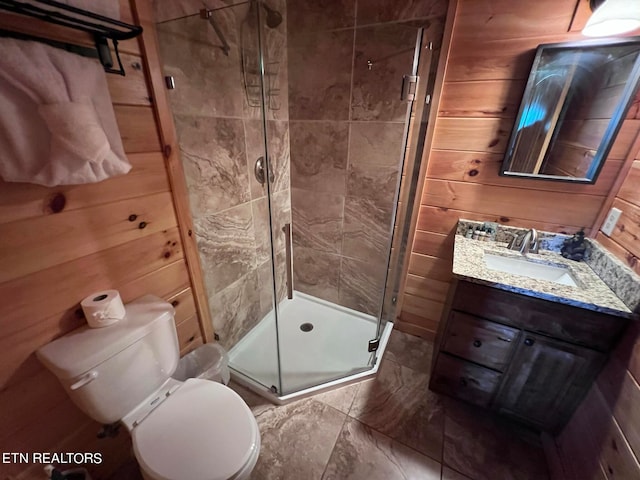 bathroom featuring an enclosed shower, vanity, toilet, and wooden walls