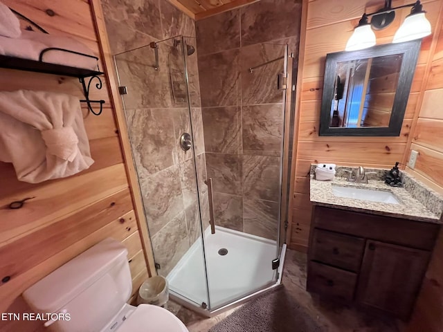 bathroom featuring wooden walls, toilet, walk in shower, and vanity with extensive cabinet space