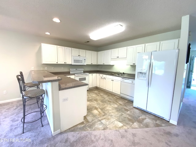 kitchen featuring light colored carpet, white appliances, kitchen peninsula, and a breakfast bar