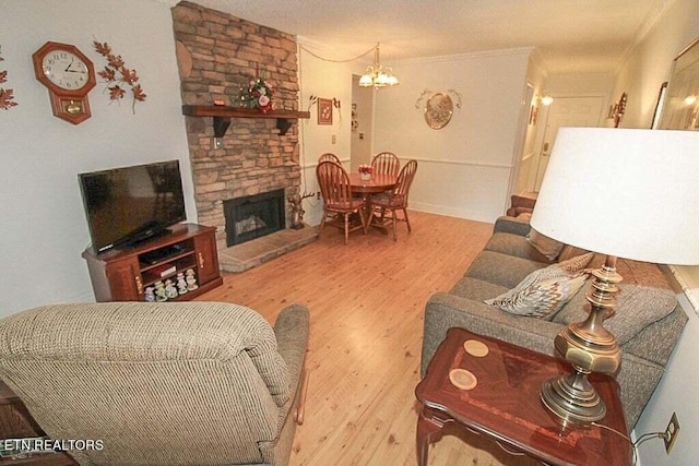 living room featuring ornamental molding, a stone fireplace, an inviting chandelier, and hardwood / wood-style floors