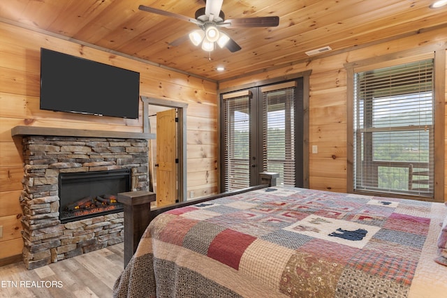 bedroom featuring access to exterior, ceiling fan, a stone fireplace, wood-type flooring, and french doors