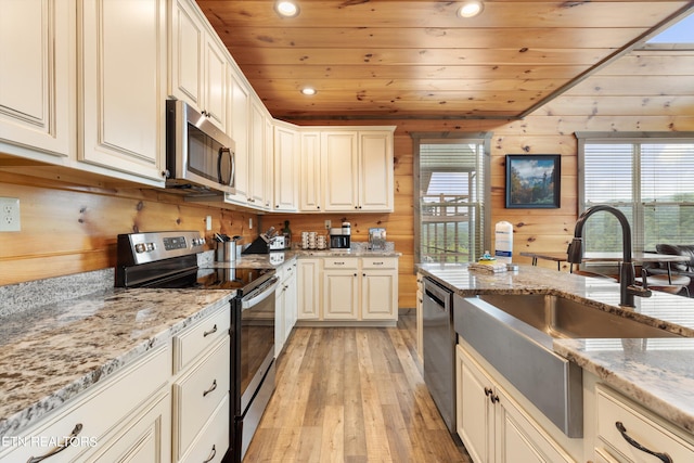 kitchen with plenty of natural light, stainless steel appliances, wood walls, and light wood-type flooring