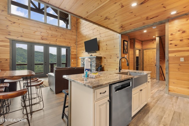 kitchen featuring a wealth of natural light, wooden walls, light wood-type flooring, and stainless steel dishwasher