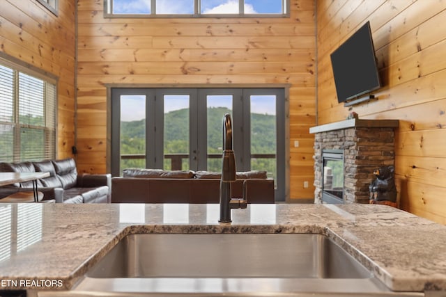 kitchen with french doors, a fireplace, light stone counters, wooden walls, and sink