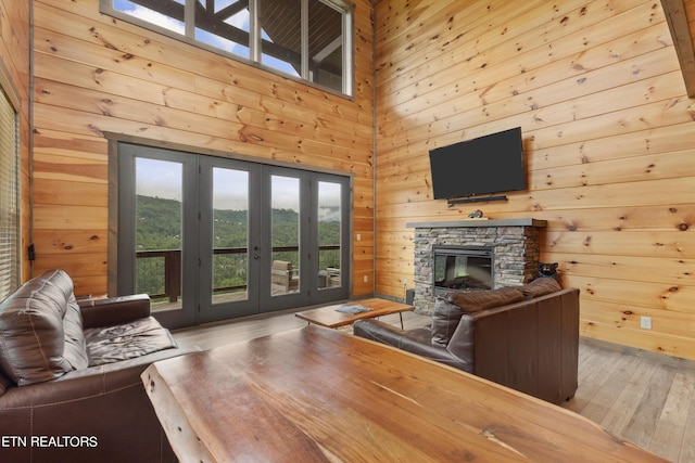 living room featuring french doors, light wood-type flooring, wood walls, a stone fireplace, and a towering ceiling