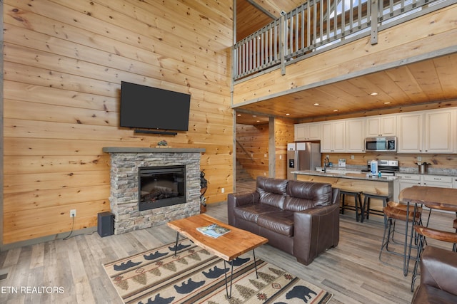 living room featuring wooden ceiling, a towering ceiling, a stone fireplace, and light wood-type flooring