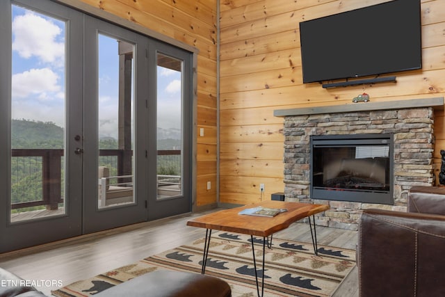 living room featuring a stone fireplace, hardwood / wood-style flooring, wood walls, and french doors