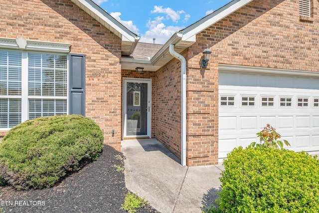 entrance to property with brick siding, an attached garage, and roof with shingles
