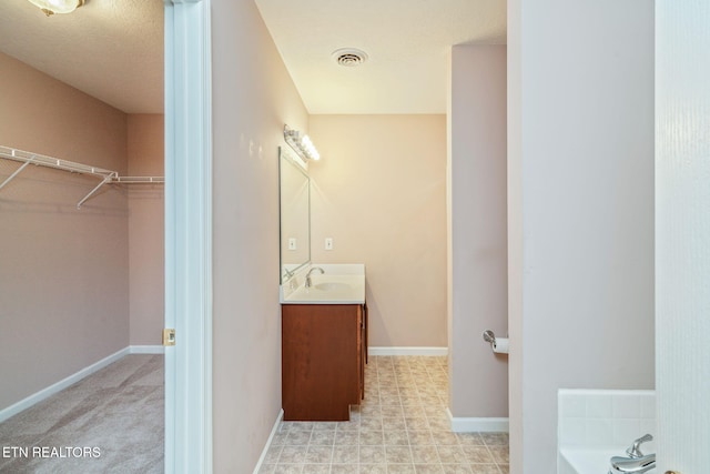 bathroom with a spacious closet, vanity, a tub to relax in, baseboards, and visible vents