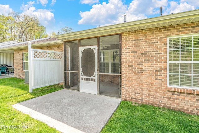 entrance to property featuring a lawn, brick siding, and a patio area