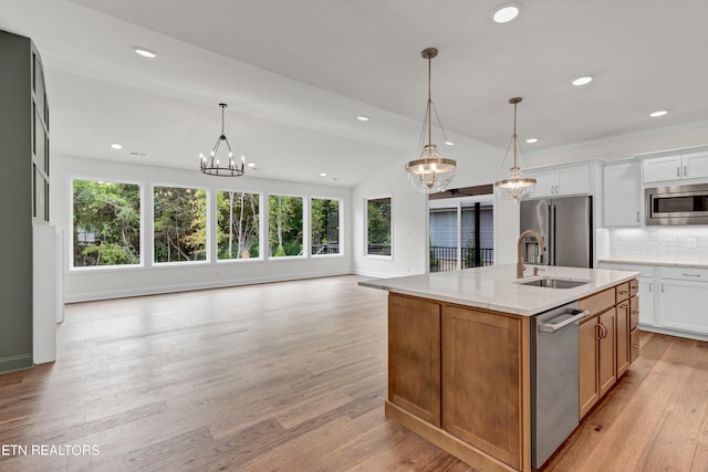 kitchen with white cabinets, appliances with stainless steel finishes, light hardwood / wood-style floors, sink, and an island with sink