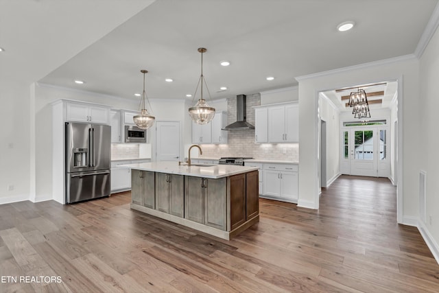 kitchen featuring appliances with stainless steel finishes, light hardwood / wood-style floors, an island with sink, wall chimney range hood, and white cabinets