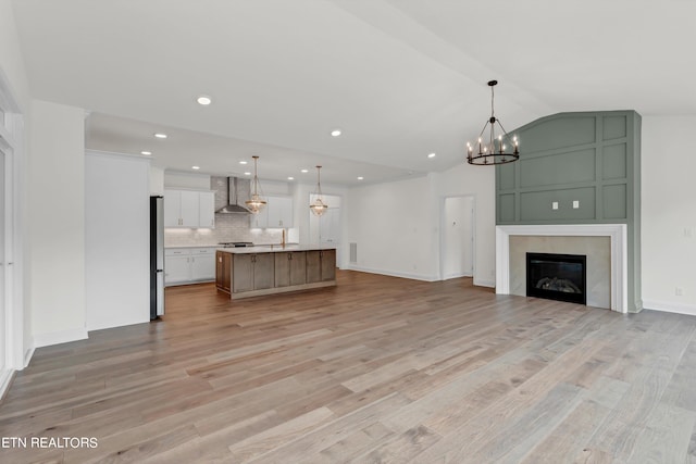 unfurnished living room with light wood-type flooring, sink, a notable chandelier, and vaulted ceiling