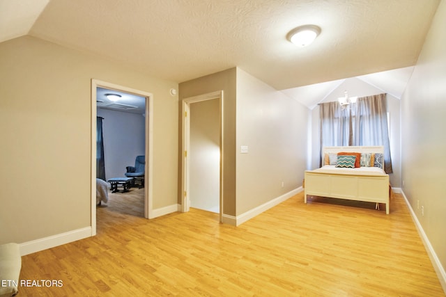 bedroom featuring a textured ceiling, light hardwood / wood-style floors, a notable chandelier, and vaulted ceiling