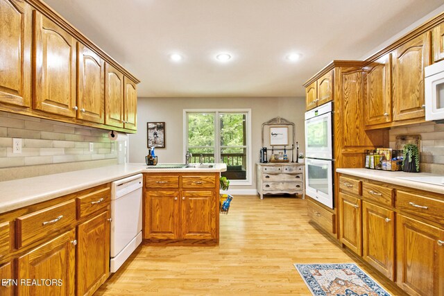 kitchen with kitchen peninsula, backsplash, white appliances, sink, and light wood-type flooring