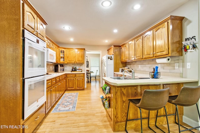 kitchen featuring a kitchen bar, light hardwood / wood-style floors, tasteful backsplash, white appliances, and kitchen peninsula