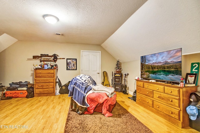 bedroom with lofted ceiling, light hardwood / wood-style flooring, and a textured ceiling