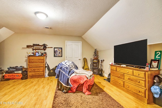 bedroom featuring a textured ceiling, lofted ceiling, and light wood-type flooring