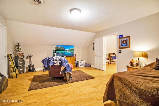 bedroom featuring lofted ceiling, light wood-type flooring, and a textured ceiling