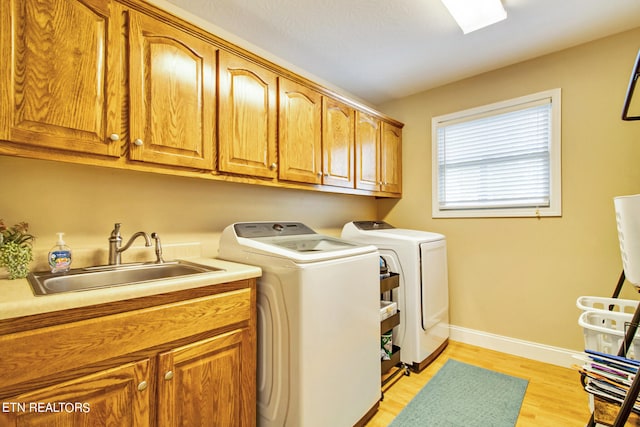 clothes washing area with light hardwood / wood-style flooring, sink, washing machine and dryer, and cabinets