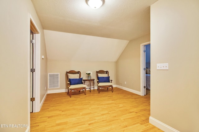 sitting room featuring lofted ceiling, light hardwood / wood-style floors, and a textured ceiling