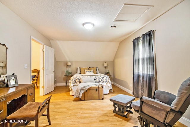 bedroom with lofted ceiling, light hardwood / wood-style flooring, and a textured ceiling