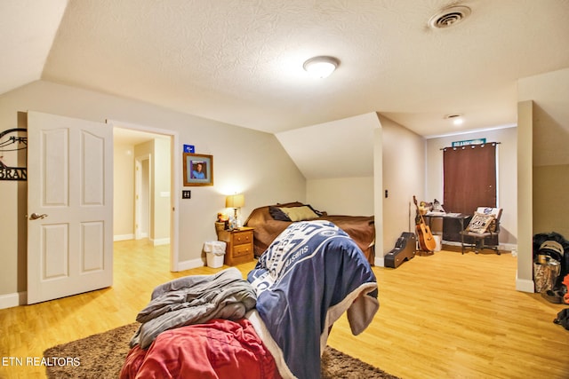 bedroom with lofted ceiling, hardwood / wood-style flooring, and a textured ceiling