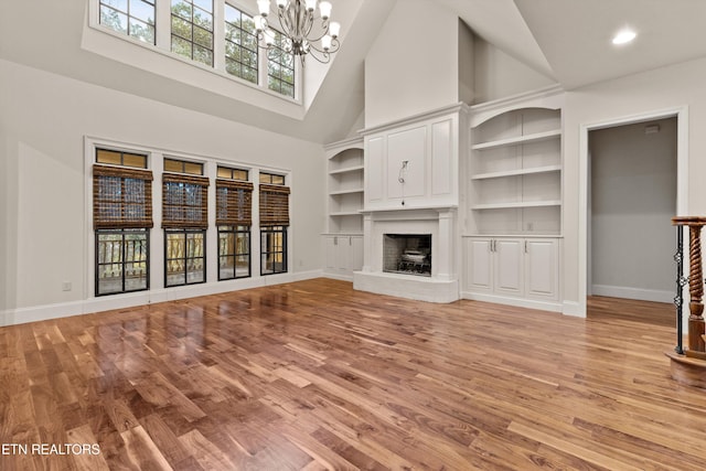 unfurnished living room featuring light wood-type flooring, built in features, high vaulted ceiling, and an inviting chandelier