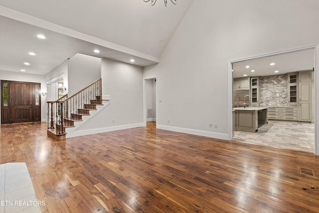 unfurnished living room featuring sink, light wood-type flooring, and high vaulted ceiling