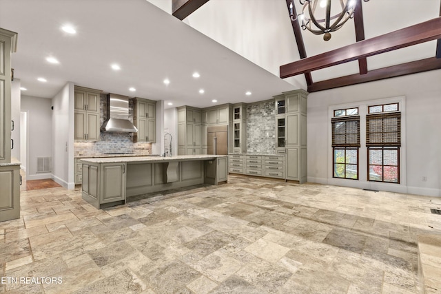 kitchen featuring an island with sink, decorative backsplash, wall chimney exhaust hood, and gray cabinets