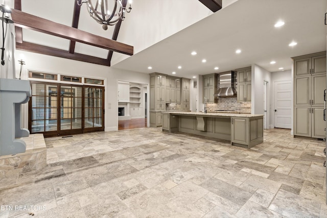 kitchen with beamed ceiling, wall chimney range hood, gray cabinetry, a large island, and decorative backsplash