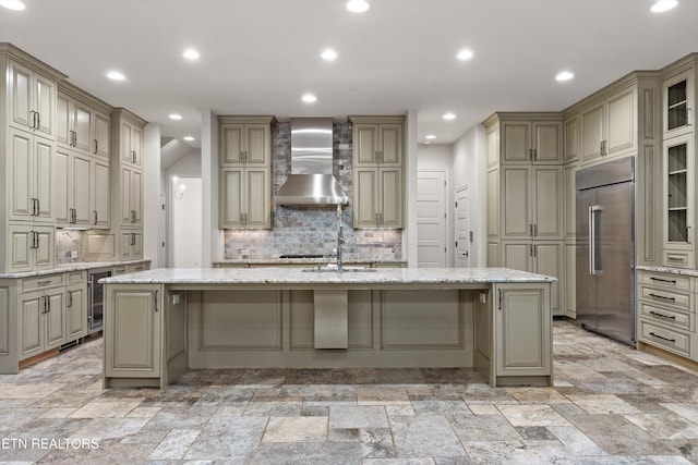 kitchen featuring wall chimney exhaust hood, beverage cooler, a kitchen island with sink, built in fridge, and decorative backsplash