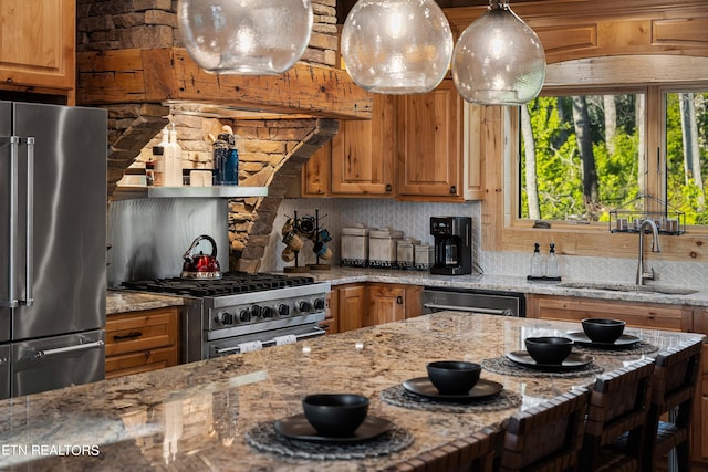 kitchen with light stone countertops, decorative light fixtures, high end appliances, sink, and backsplash