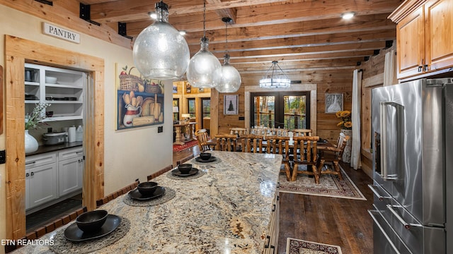 kitchen featuring high end refrigerator, beamed ceiling, wooden walls, hanging light fixtures, and light stone countertops
