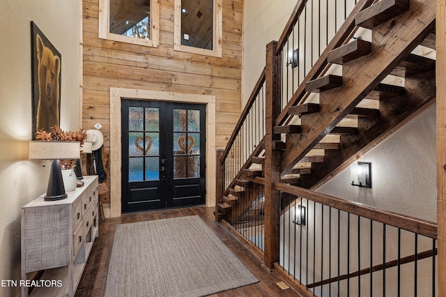 entrance foyer featuring french doors, a towering ceiling, dark hardwood / wood-style flooring, and wood walls