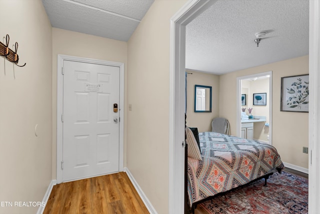 bedroom featuring a textured ceiling, light hardwood / wood-style floors, and connected bathroom