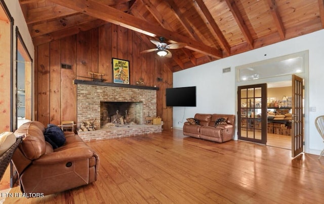 living room featuring wood walls, light hardwood / wood-style flooring, ceiling fan, beam ceiling, and a fireplace