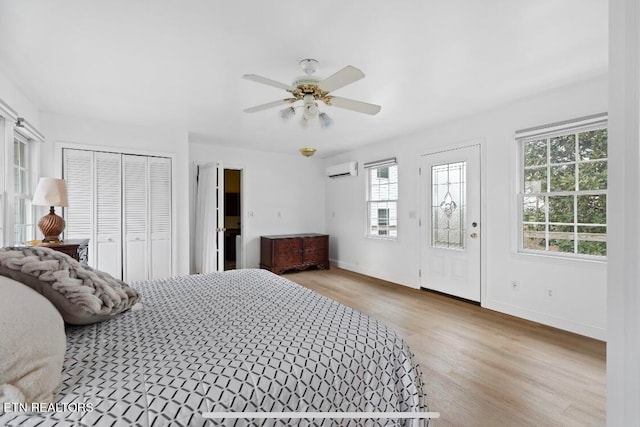 bedroom with multiple windows, ceiling fan, a wall mounted AC, and light wood-type flooring