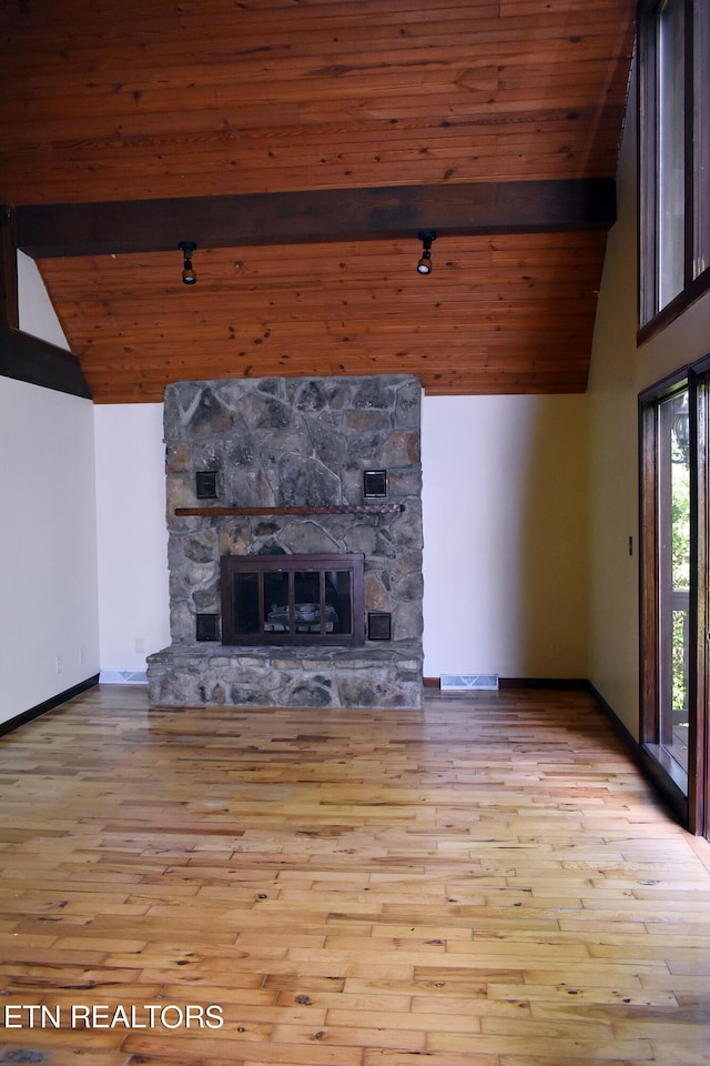 unfurnished living room with high vaulted ceiling, a stone fireplace, beam ceiling, wooden ceiling, and light wood-type flooring