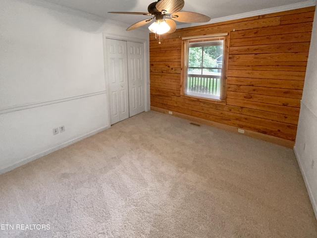 unfurnished bedroom with ornamental molding, wooden walls, a closet, carpet, and ceiling fan