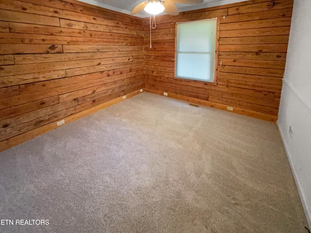 carpeted empty room with wood walls, ceiling fan, and crown molding