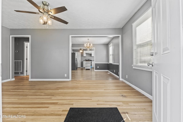 unfurnished living room with ceiling fan with notable chandelier and light hardwood / wood-style flooring