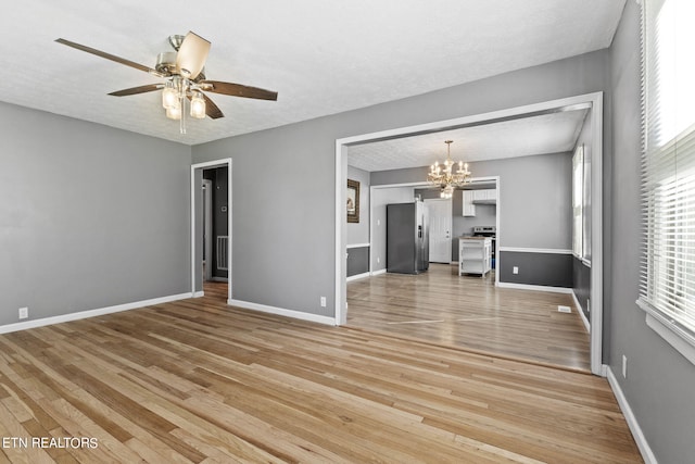 unfurnished living room with ceiling fan with notable chandelier, a healthy amount of sunlight, light hardwood / wood-style floors, and a textured ceiling