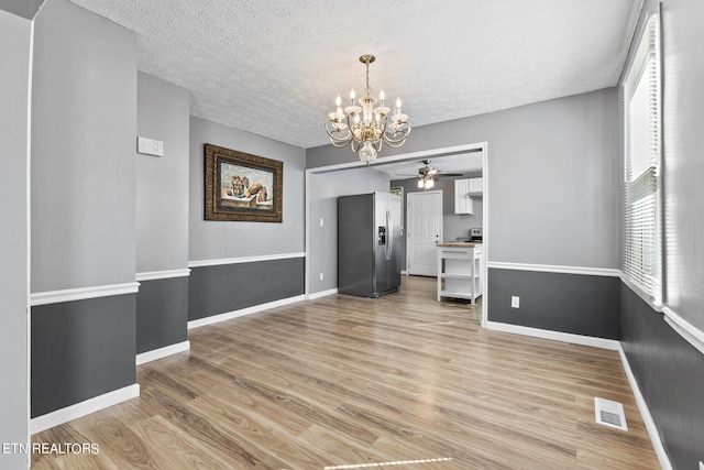 unfurnished dining area with a textured ceiling, ceiling fan with notable chandelier, and hardwood / wood-style floors