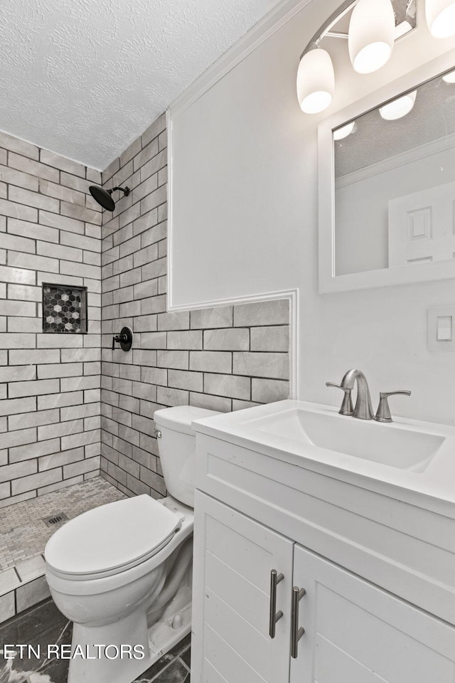 bathroom featuring tiled shower, oversized vanity, toilet, tile flooring, and a textured ceiling