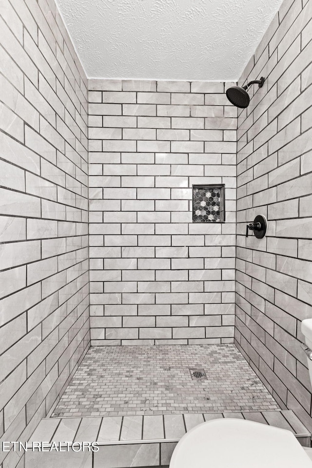 bathroom with tiled shower and a textured ceiling