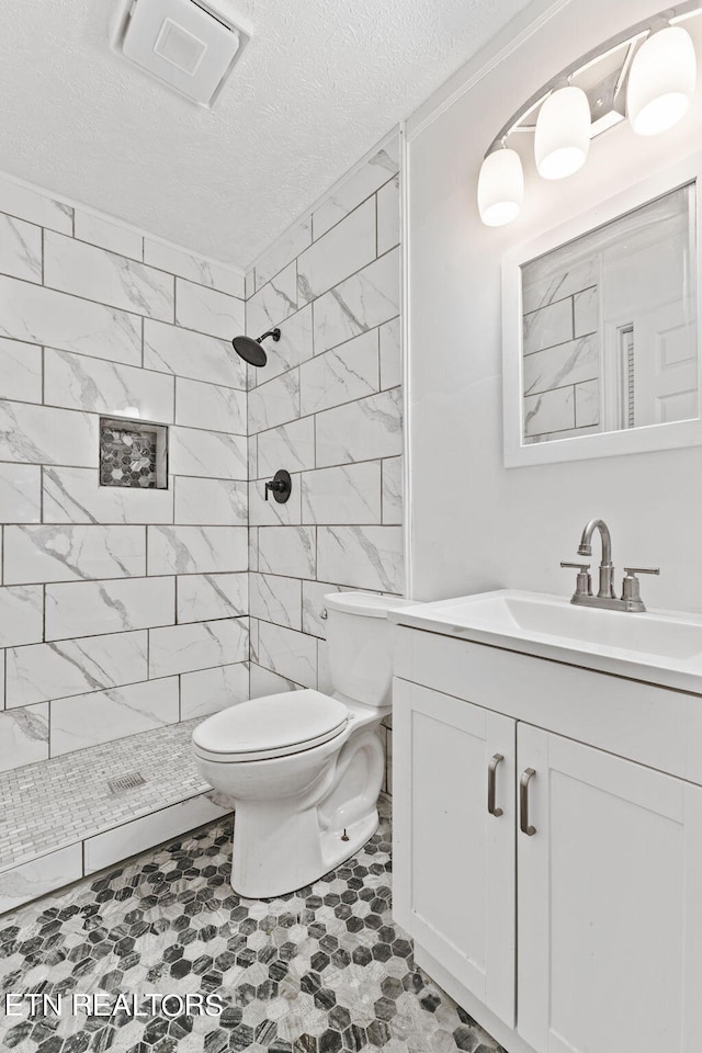 bathroom featuring tiled shower, a textured ceiling, tile floors, toilet, and vanity