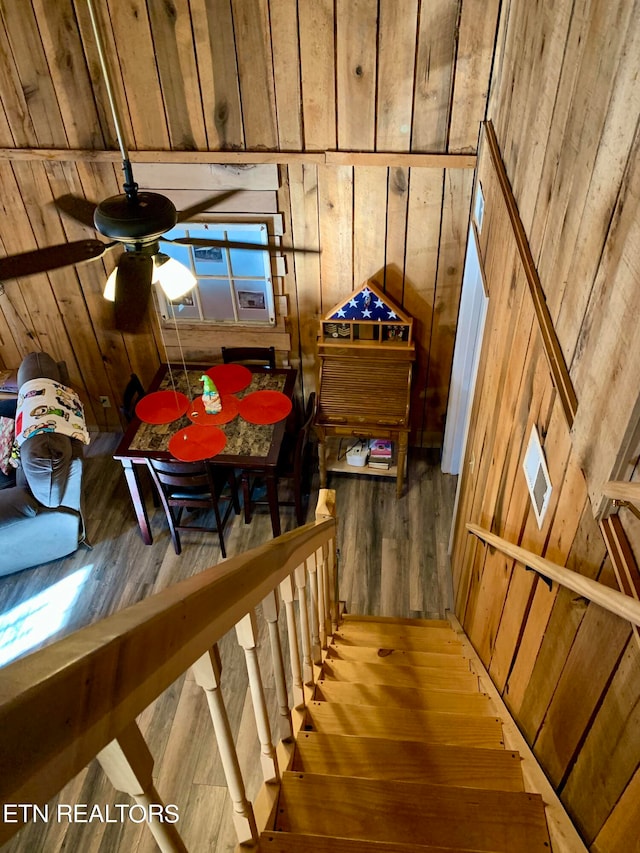 staircase featuring wooden walls, ceiling fan, and wood-type flooring